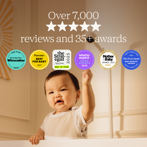 Baby standing on a step stool with award badges displayed above, set against a neutral background.